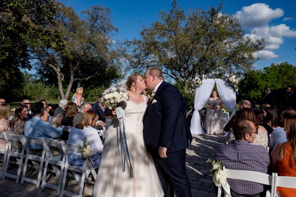 bride and groom kissing after their outdoor wedding ceremony with guests in background